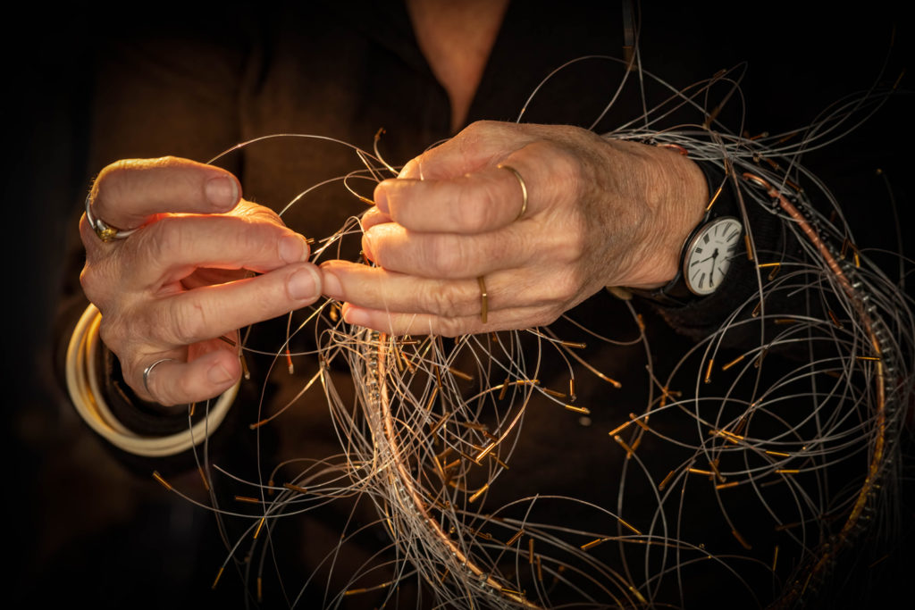 Kirsten Sonne's hands with a large bundle of copper wire around her wrists. She is weaving the stands together.