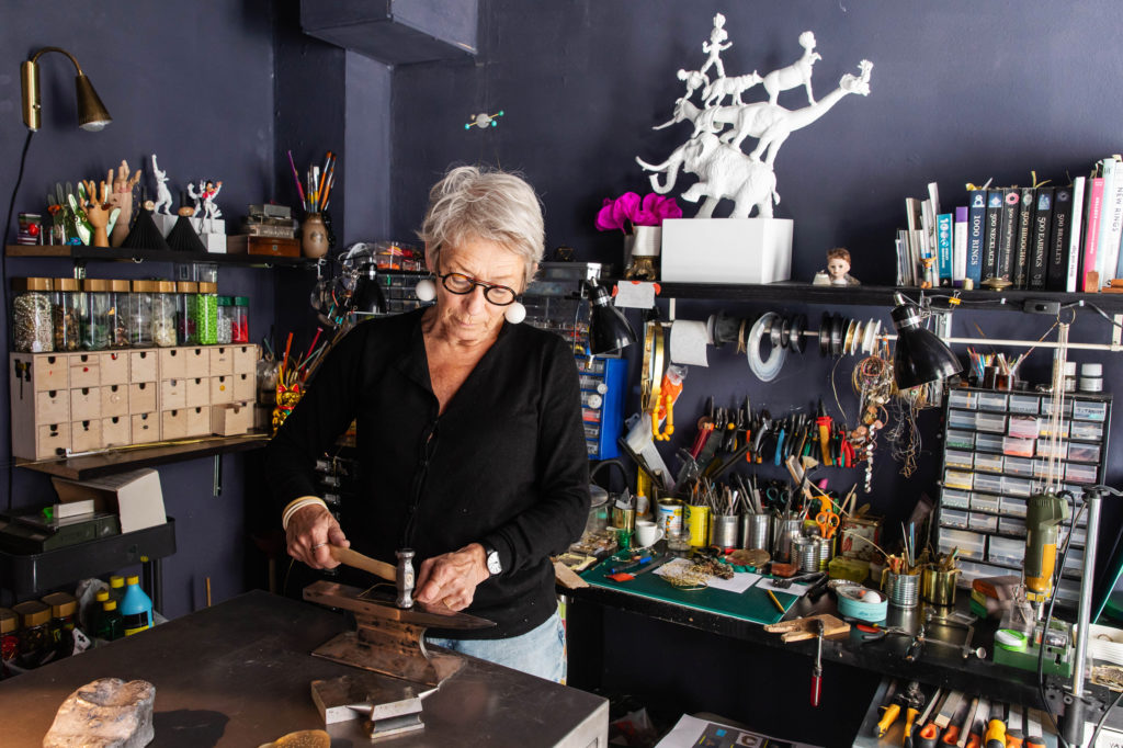 Sonne, wearing all black, working in her studio. Hammering wire on an anvil.