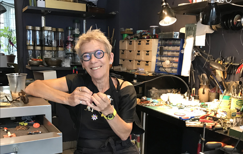 Kirsten Sonne sat in the middle of the frame, in her workshop. Wearing black clothes and apron.